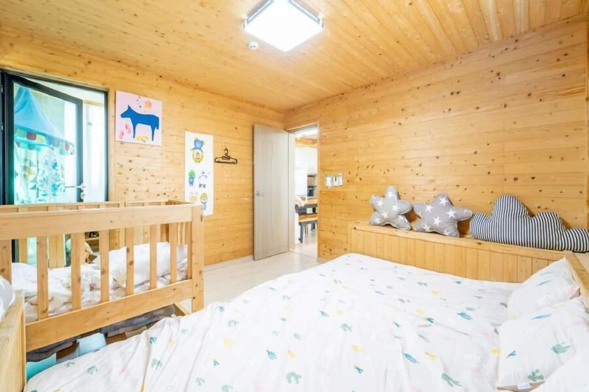A wooden room with a bed, a crib, and a door leading to another room.