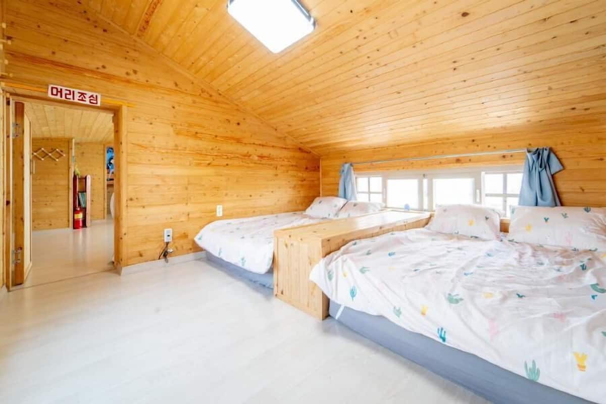 A wooden cabin with two beds, a window, and a door labeled '아리조선'.
