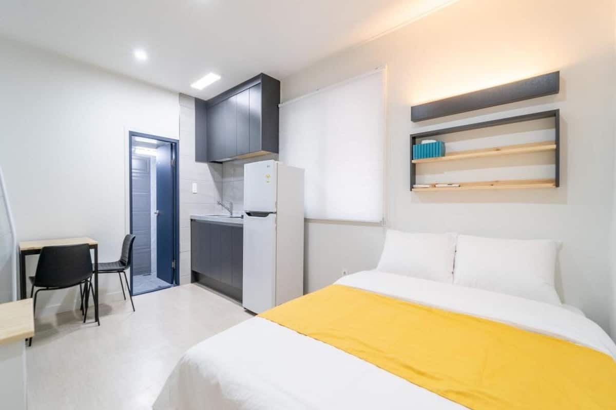 Ein Hotelzimmer mit einem Bett, einem Schreibtisch, einem Stuhl, einer Küchenzeile und einem Bücherregal.