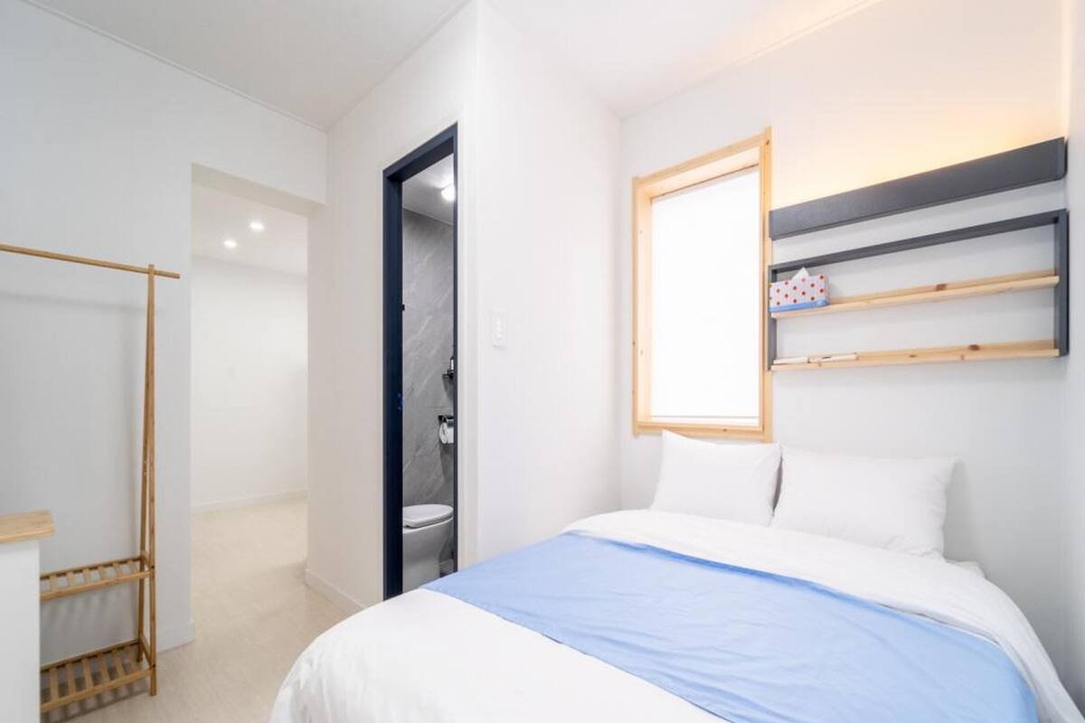 Ein modernes Schlafzimmer mit Bett, einem Holzschrank, einem Badezimmer mit Dusche und einem Spiegel an der Wand.