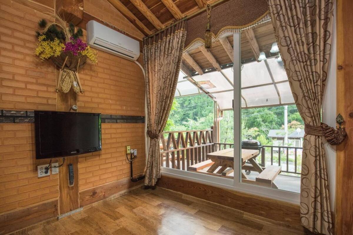 A wooden interior with a TV, air conditioning, and a view to an outdoor deck.