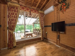 A wooden interior with a TV mounted on the wall, a wooden bench outside, and a view of greenery through large windows. - Gapyeong Supsokui Harmony Pension (Gapyeong)