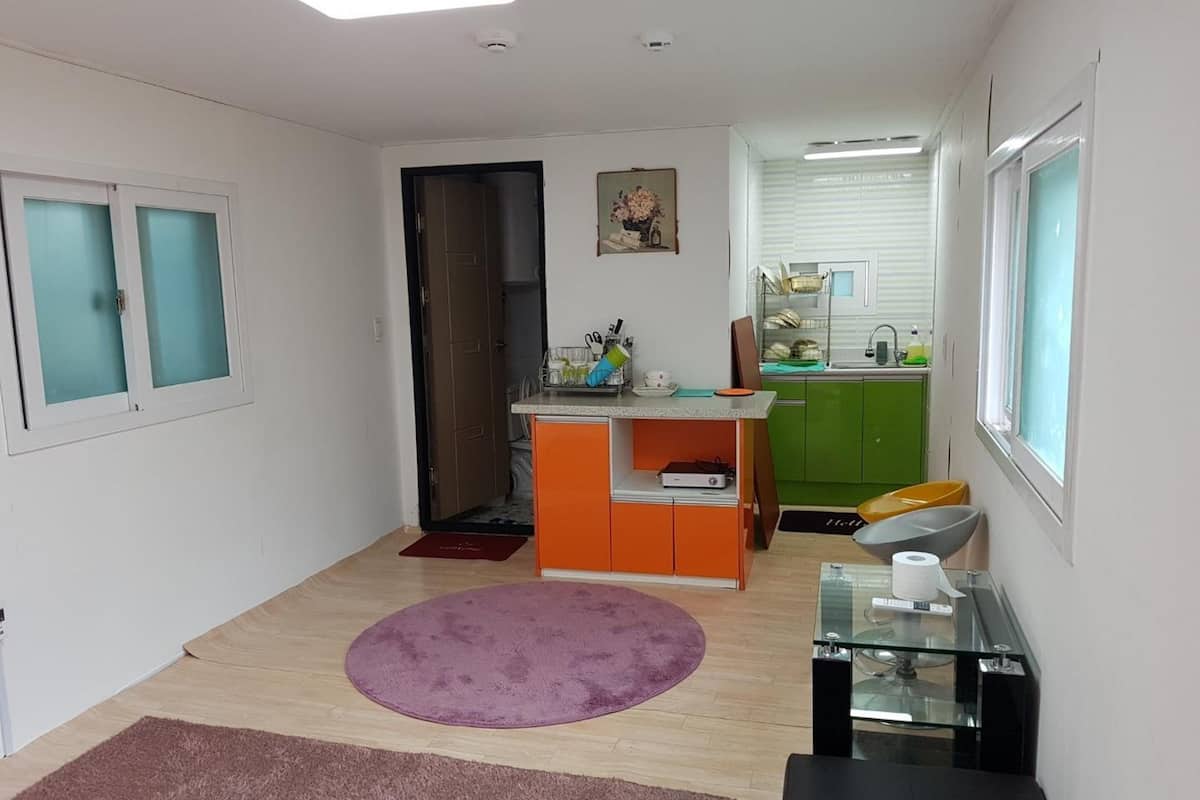 Un espace de vie compact comprenant un coin cuisine, un tapis violet et une table en verre.