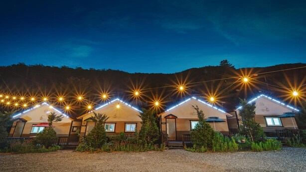 A row of cabins with string lights and a gravel driveway. - Hongcheon Daebakine Pension (Hongcheon)