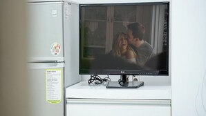 A television mounted on a white cabinet with a small refrigerator to its left. - Hongcheon Daebakine Pension (Hongcheon)