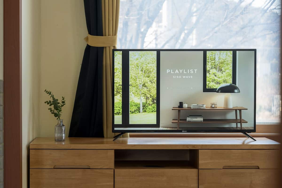 A modern room with a wooden desk, a vase with a plant, and a window with a view of greenery.