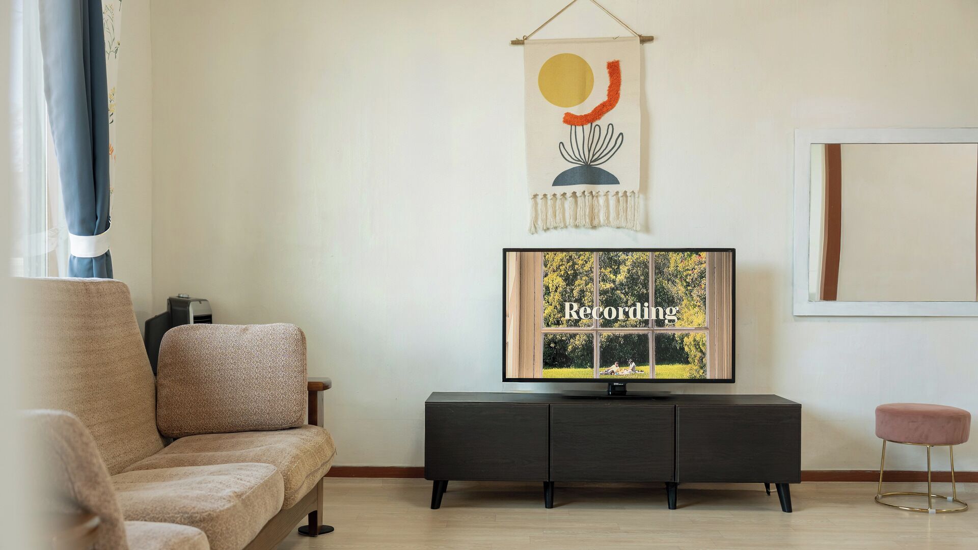 A living room with a sofa, a TV on a stand, a small stool, and a wall-mounted artwork.