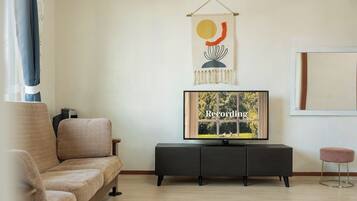 A living room with a sofa, a TV on a stand, a small stool, and a wall-mounted artwork.