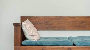 Ein hölzernes Bett mit blauer Decke und einem Kissen mit Muster an einer schlichten Wand.