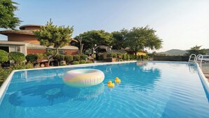A swimming pool with a floating ring and rubber ducks, surrounded by trees and buildings. - Daebudo Banditbul Pension (Ansan)