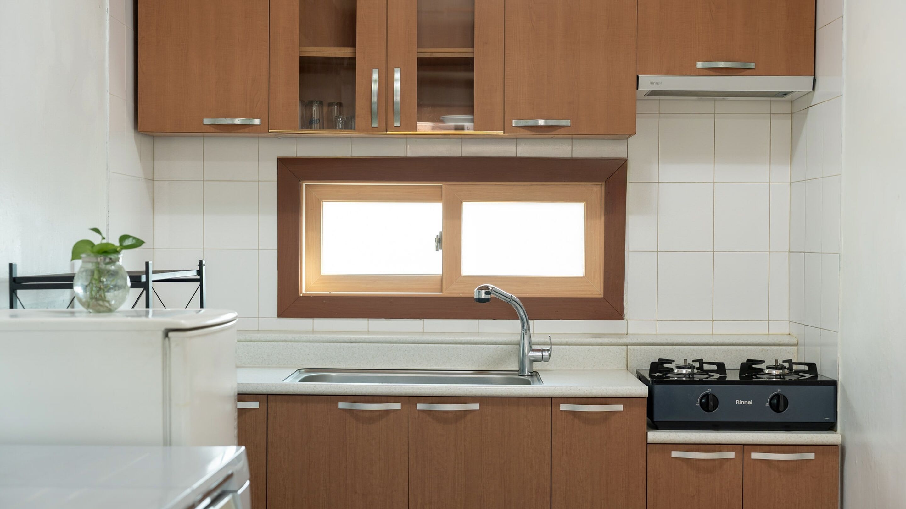 A kitchen with wooden cabinets, a window above the sink, a gas stove, and a plant on the counter.