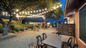 An outdoor seating area with tables and chairs, string lights, and a building with a sign. - Daebudo Banditbul Pension (Ansan)