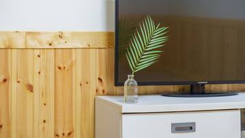 Un televisor de pantalla plana sobre un mueble blanco con un florero de vidrio que contiene una planta verde.