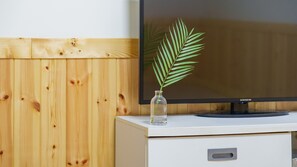A flat-screen TV on a white cabinet with a glass vase containing a green plant. - Taean Jiyu Ne Pension (Taean)