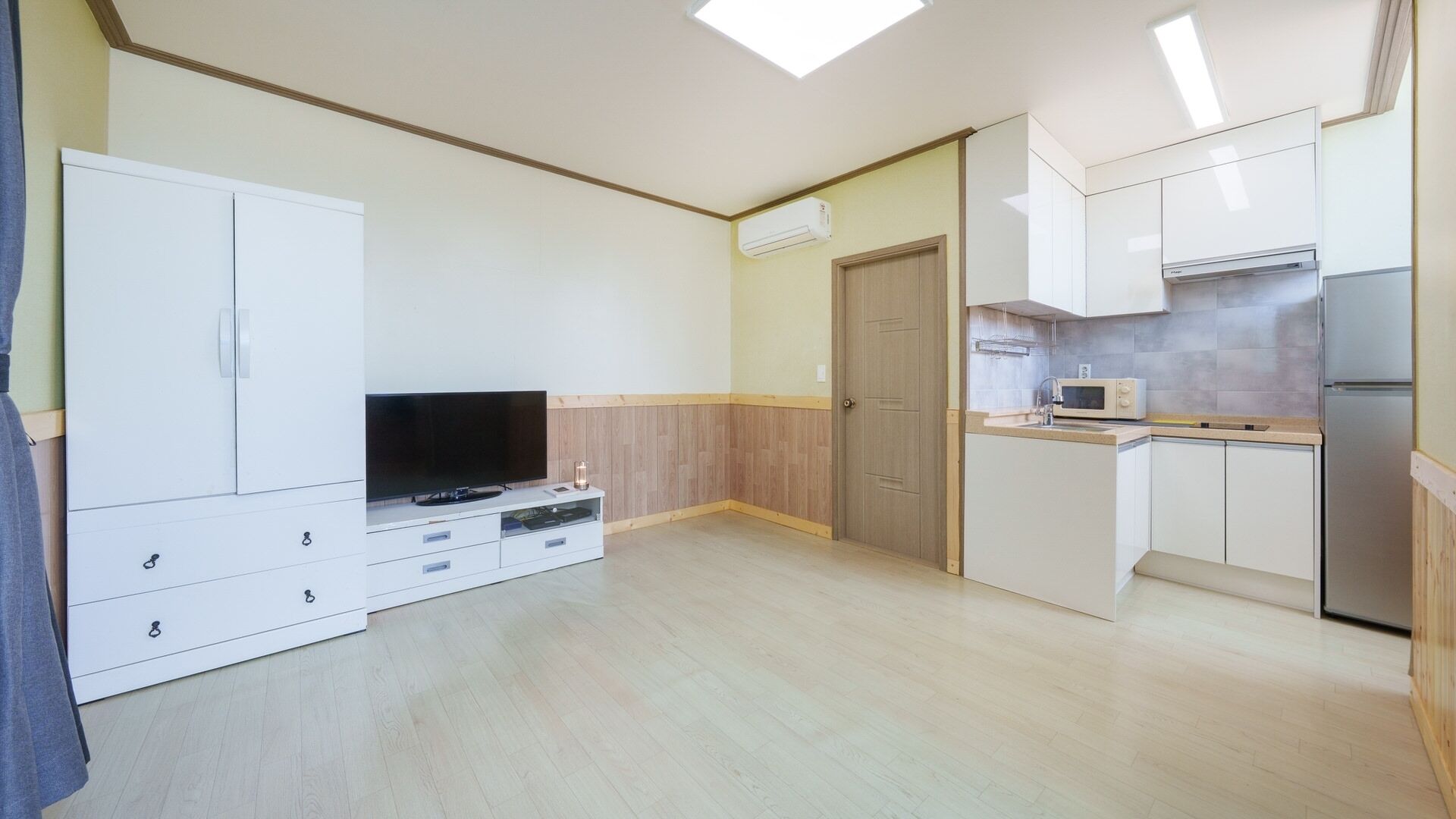 A compact living space with a TV, kitchenette, and wooden flooring.