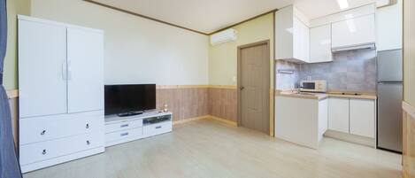 A compact living space with a TV, kitchenette, and wooden flooring.
