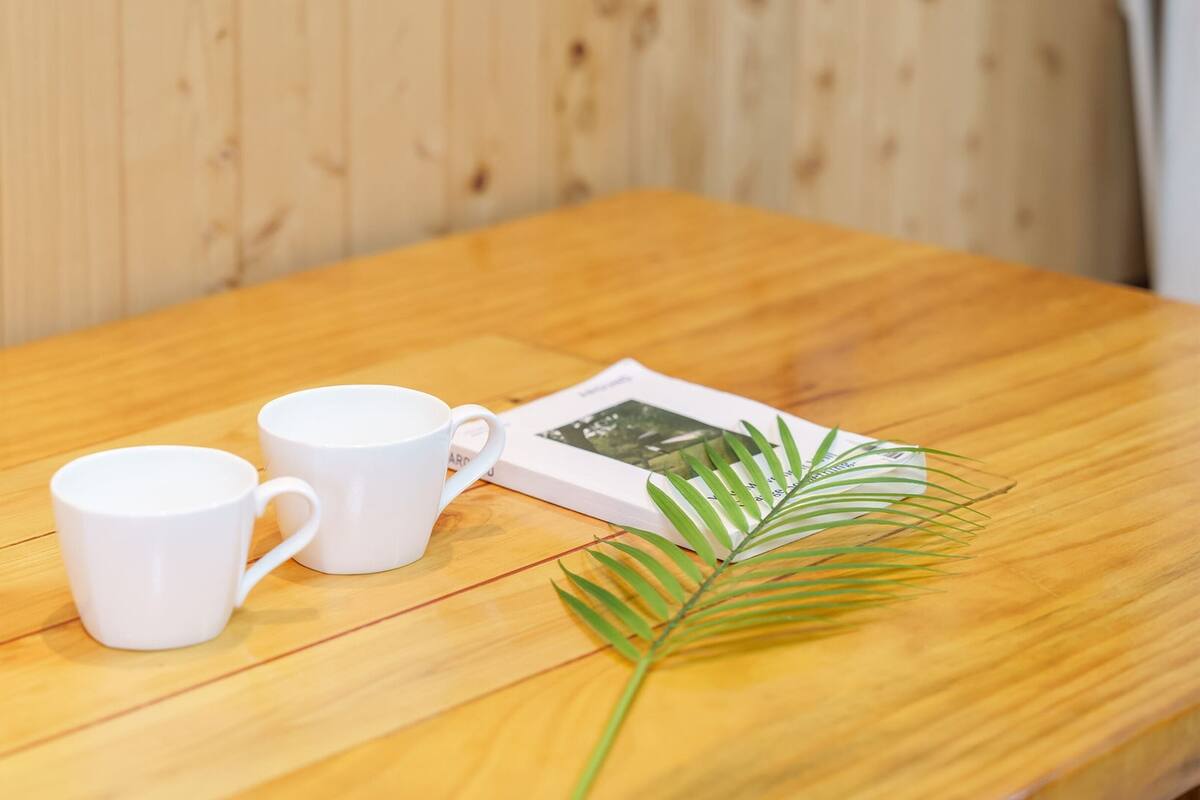 Two white mugs on a wooden table with a magazine and a green palm leaf.