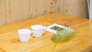 Two white mugs on a wooden table with a magazine and a green palm leaf. - Taean Jiyu Ne Pension (Taean)