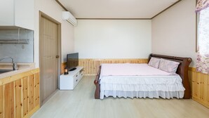 Una camera da letto con un letto in legno, una TV su una cassettiera bianca, un armadio in legno e un angolo cottura con lavello e condizionatore.