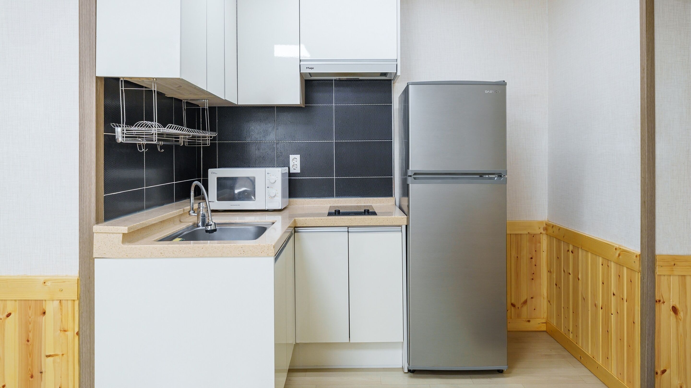 Una cocina compacta con microondas, refrigerador, lavamanos y armarios de madera.