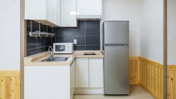 Una cocina compacta con microondas, refrigerador, lavamanos y armarios de madera.
