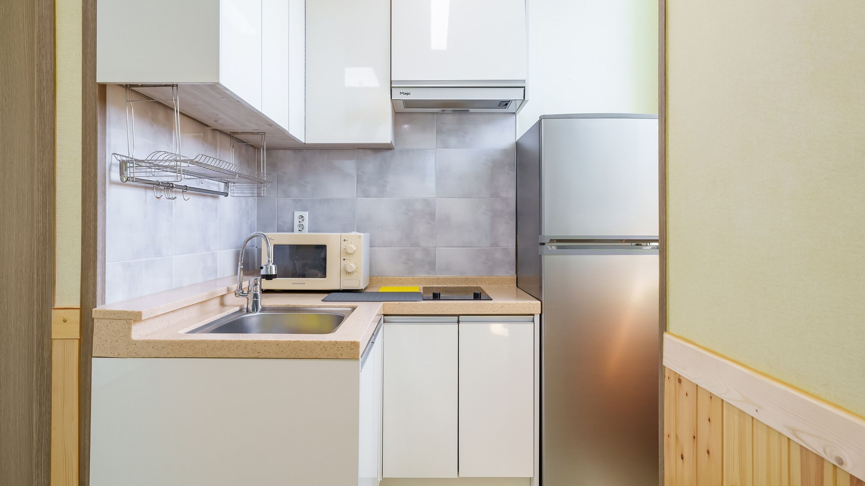 A compact kitchen with a microwave, sink, and stainless steel refrigerator.
