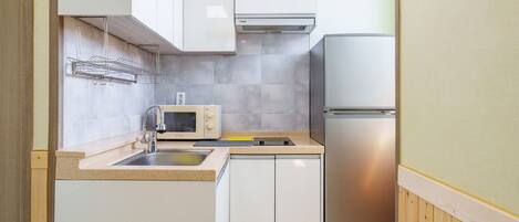 A compact kitchen with a microwave, sink, and stainless steel refrigerator.