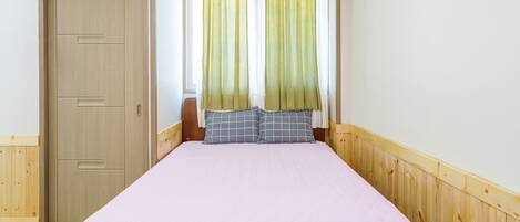 Un letto singolo con copripiumino rosa e due cuscini, un armadio in legno e una finestra con tende verdi.