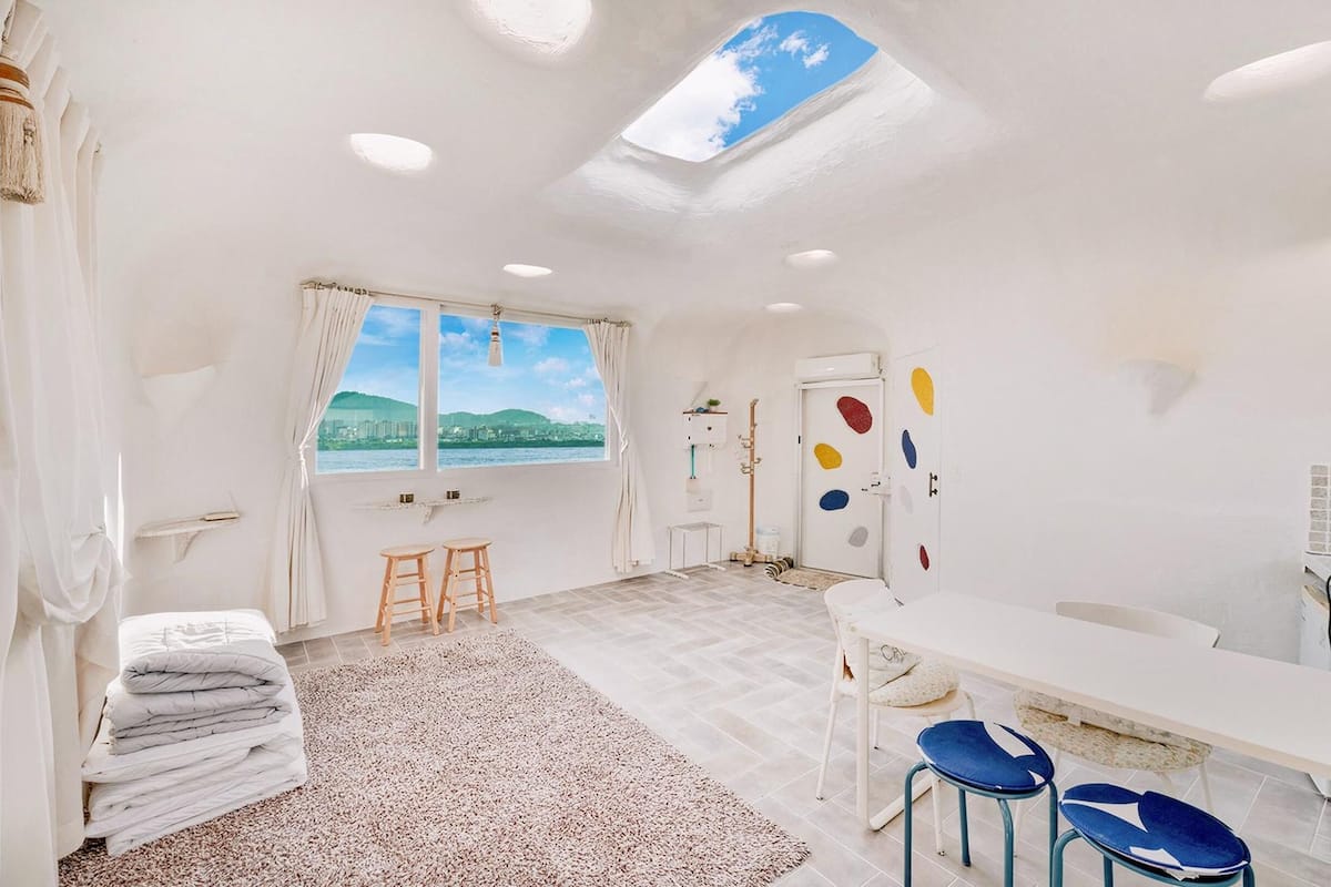Habitació ampla i clara, amb finestra gran, tragèta al sostre i bany que inclou un vàter blanc i decoracions murals de colors.