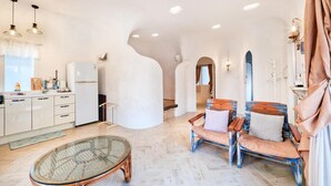 A modern kitchen with white cabinets, a refrigerator, and a dining area with a wicker table and two wooden chairs. - Jeju Mulgogi Pension (Jeju City)