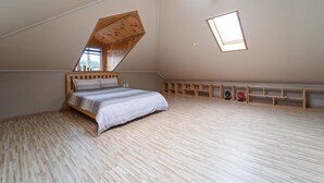 Une chambre avec un plafond en pente, un lit, un puits de lumière et des étagères en bois intégrées le long du mur.