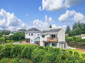 Een herenhuis met balkon, omgeven door weelderige begroeiing en een helderblauwe lucht.