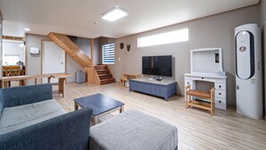 Un salon moderne avec un escalier, un téléviseur à écran plat, un réfrigérateur blanc et un coin repas avec des meubles en bois.