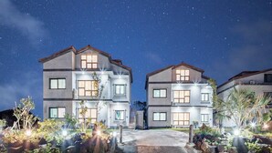 A modern two-story residential building with a well-lit entrance and landscaped garden.