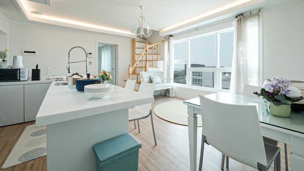 A modern kitchen with a central island, a dining area with a round table, and a view of the city through large windows.