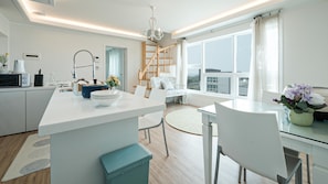 Una cocina moderna con una isla central, un comedor con mesa redonda y vistas a la ciudad a través de grandes ventanales.