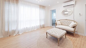 A room with a large window, a sofa, an ottoman, and a mirror on the wall.