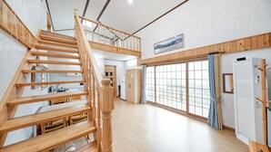 Una habitación amplia con una escalera de madera que lleva a un nivel superior, un ventanal con vistas y un equipo de aire acondicionado integrado.