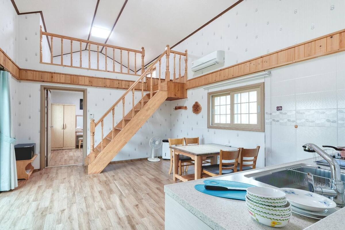 A spacious kitchen with a wooden staircase, a dining area, and a view of the adjacent room.