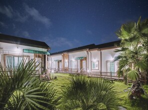 A hotel with a covered outdoor area, palm trees, and a starry night sky. - Jeju Kkumkkuneun Jeju Pension (Seogwipo)