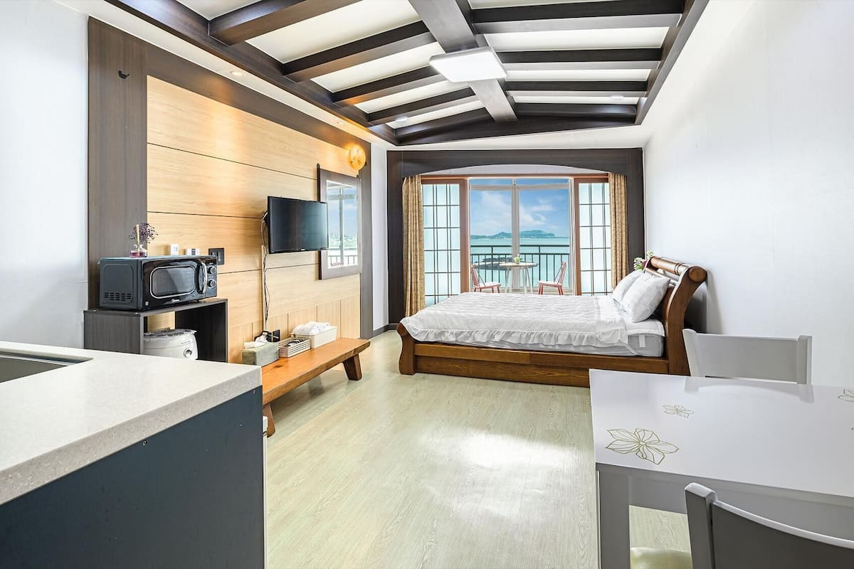 A modern bedroom with a bed, a TV, a small kitchenette, and a balcony with a view.