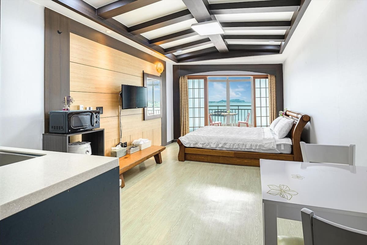 A modern hotel room with a bed, a TV, a small kitchen area, and a balcony with a view.
