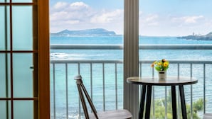 A balcony with a view of the sea, a chair, and a table with flowers. - Jeju Padosoriminbak Pension (Jeju City)