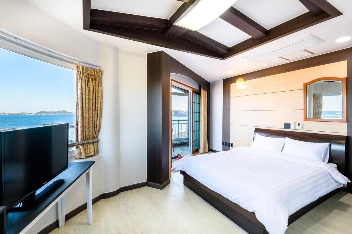 A hotel room with a large bed, a TV, and a view of the sea.