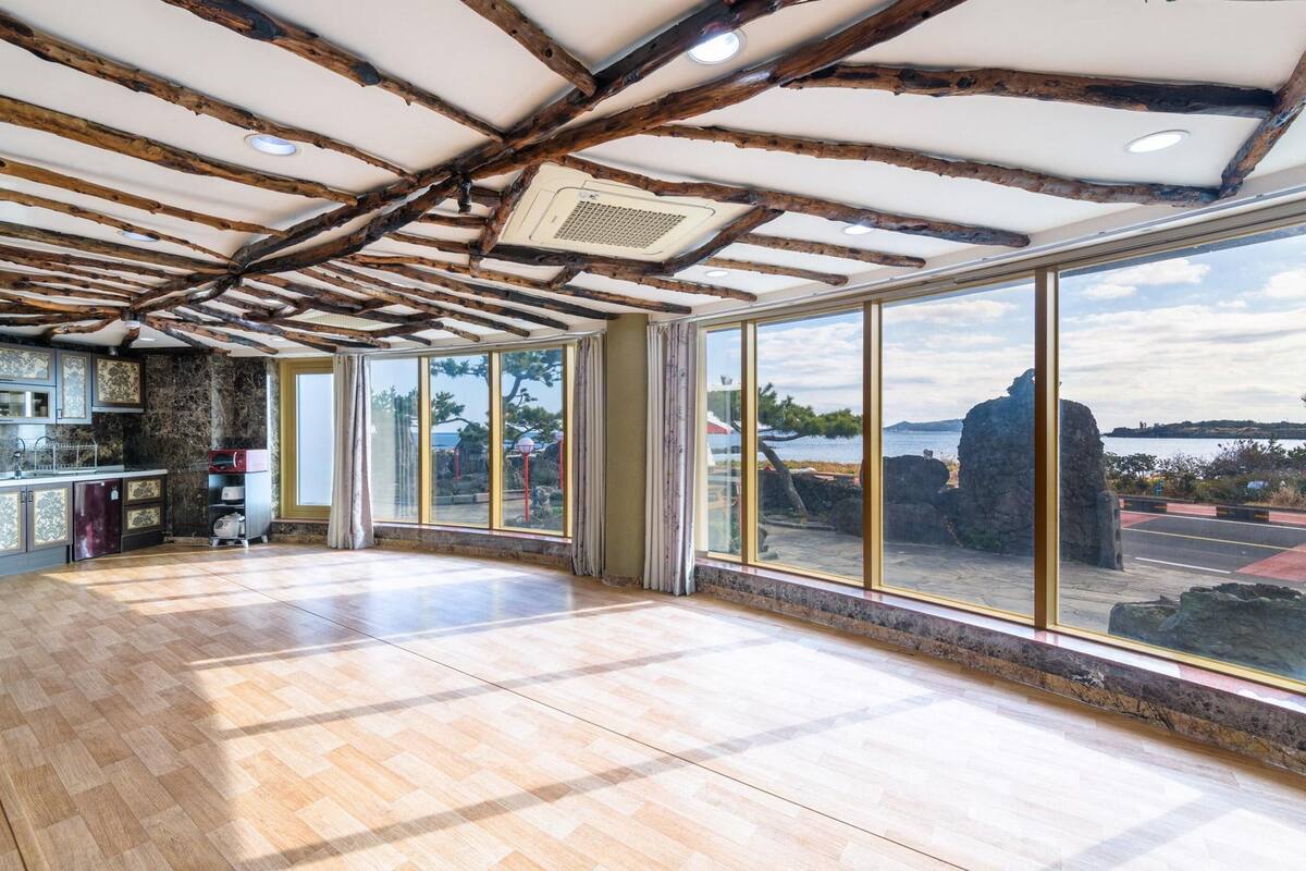 A spacious room with a wooden ceiling, large windows with a view of the sea, and a kitchen area with marble countertops.