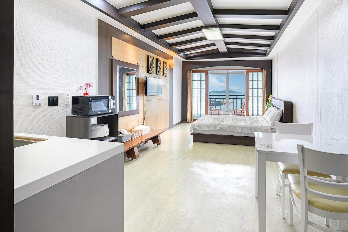 A modern hotel room with a bed, a desk, and a view of the sea.