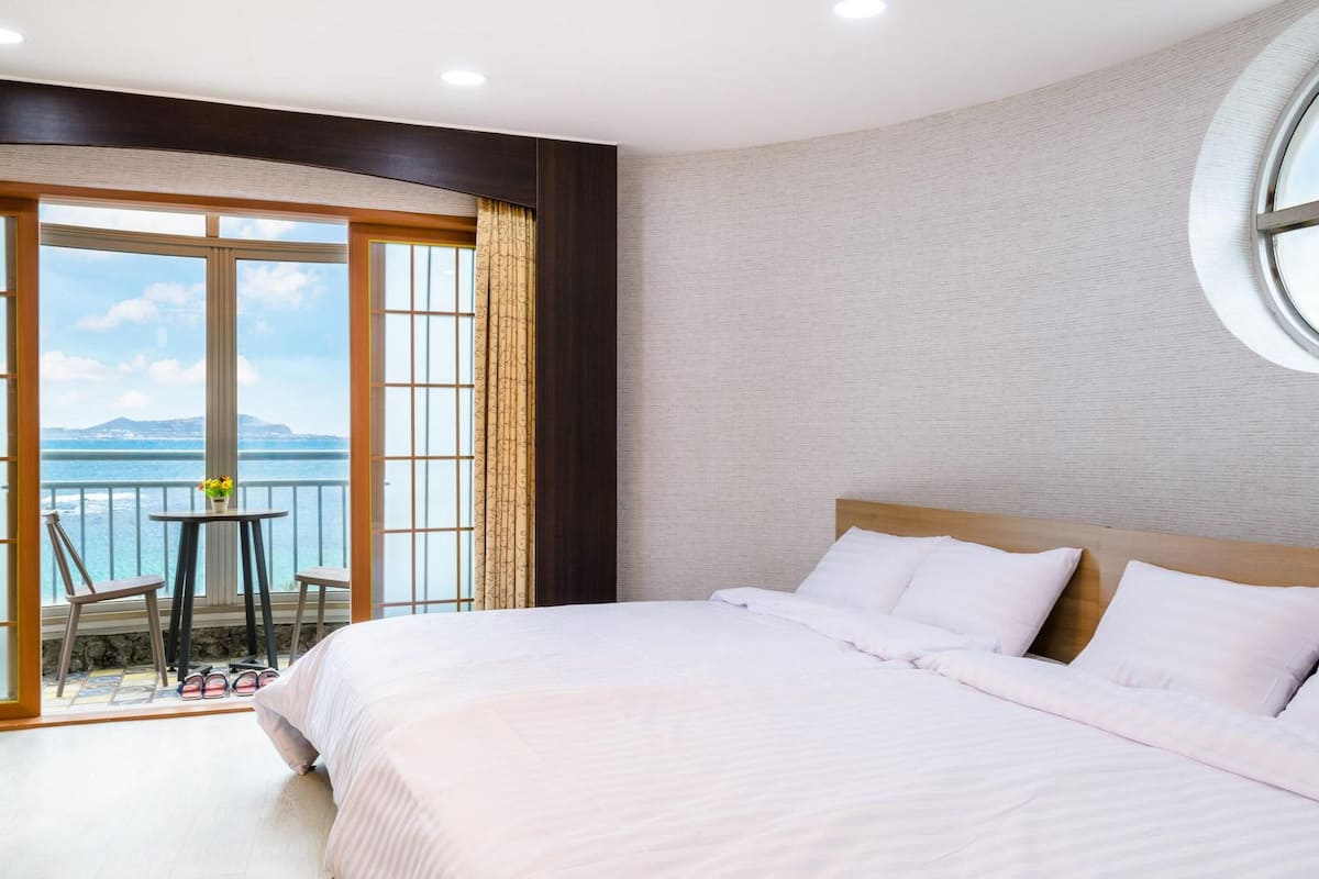 A hotel room with a large bed, a balcony with a table and chairs, and a view of the sea.