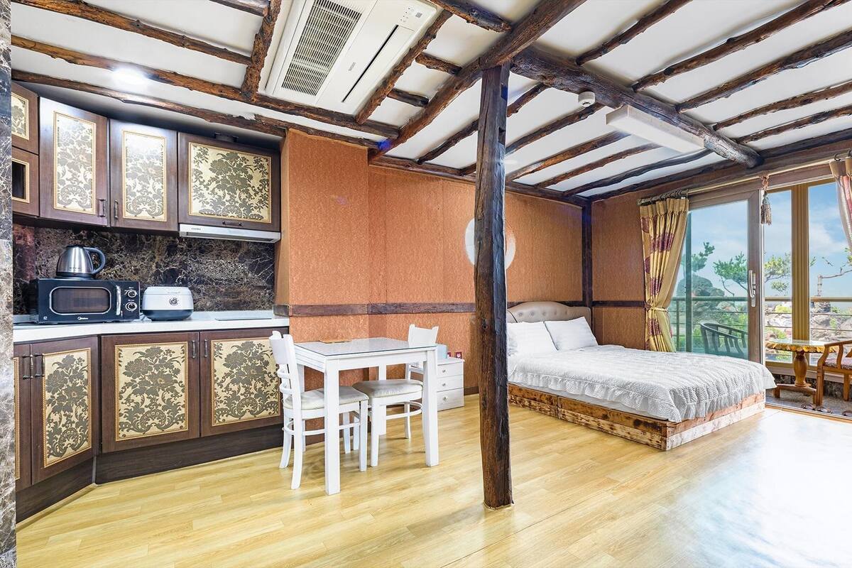 A compact room with a bed, a small table with chairs, a kitchenette with a microwave, and a view through a large window.