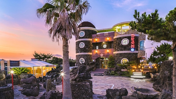 A hotel with a unique stone facade, multiple windows, and a well-lit entrance area. - Jeju Padosoriminbak Pension (Jeju City)