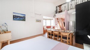 Quarto com uma cama, uma escrivaninha e uma cadeira. Há uma janela e uma porta.